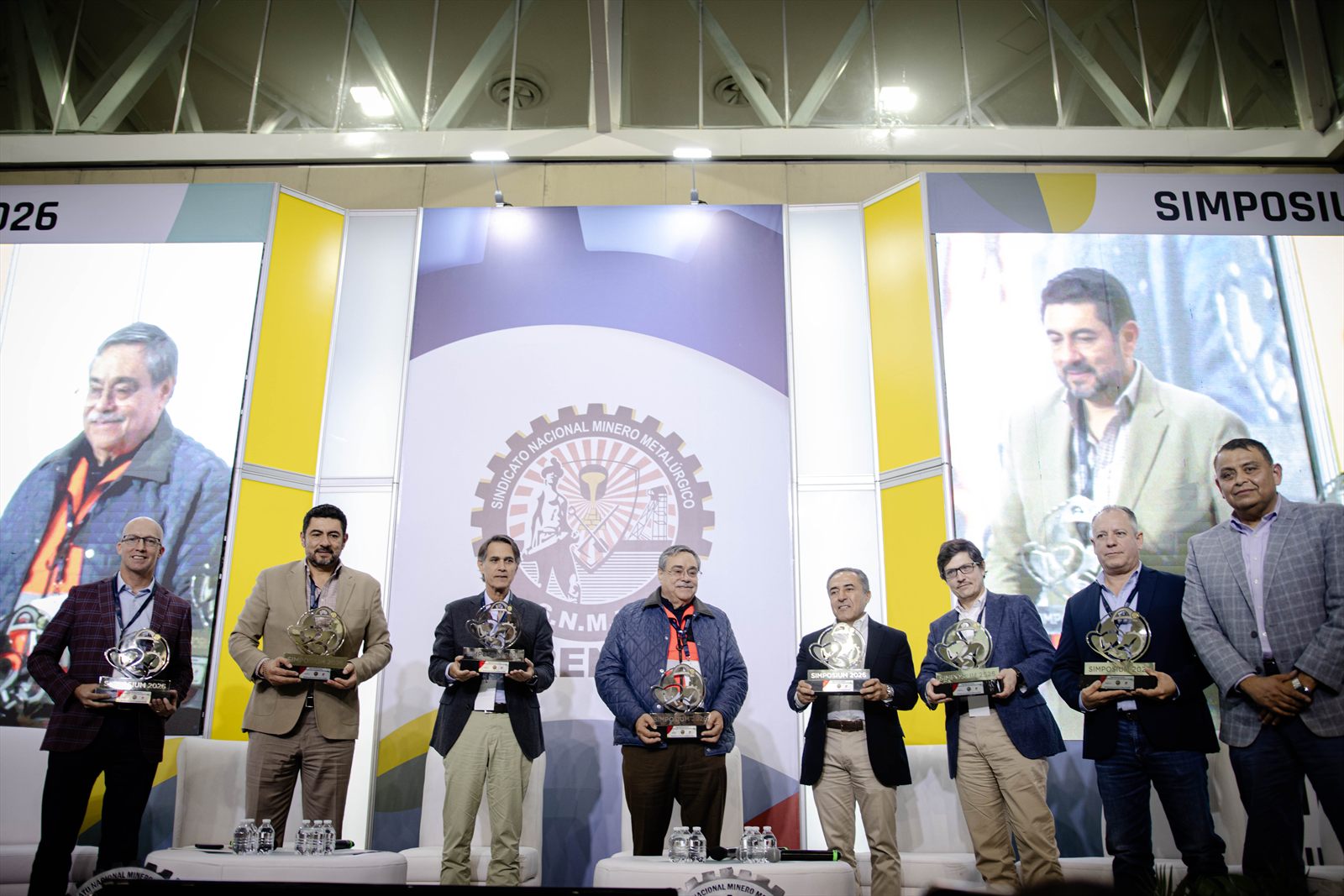 Entrega de reconocimientos en el escenario del simposio, con las personas premiadas formadas
