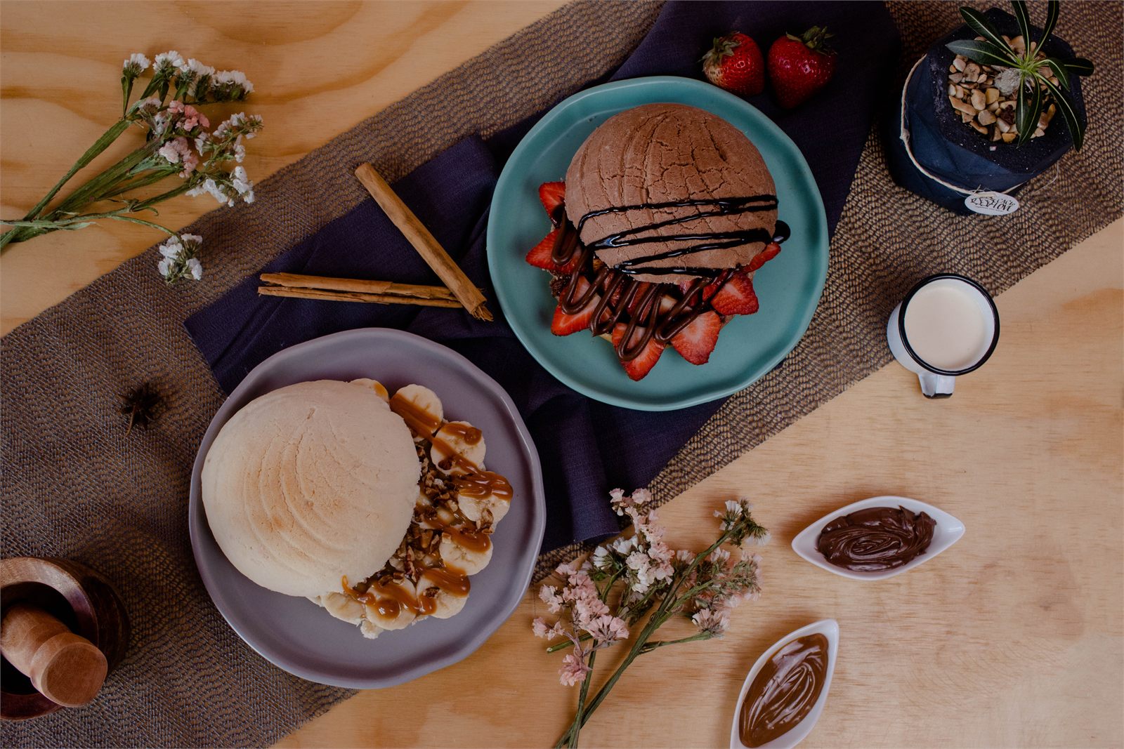 Pan dulce, fresas, chocolate y leche en una mesa con flores, vista cenital