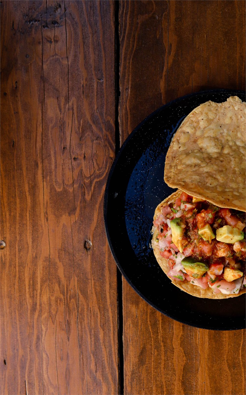 Tostada con ceviche y aguacate sobre plato negro, vista cenital