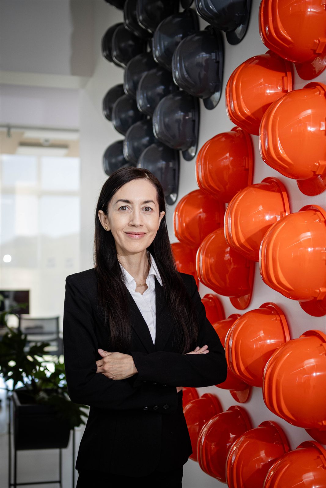 Retrato corporativo de pie frente a un muro de cascos de seguridad
