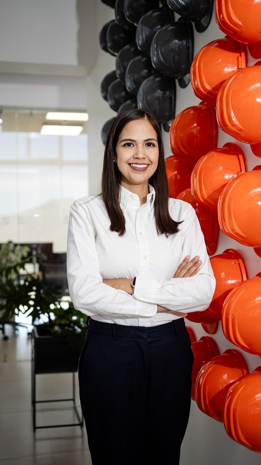 Retrato corporativo junto al muro de cascos naranjas de la oficina