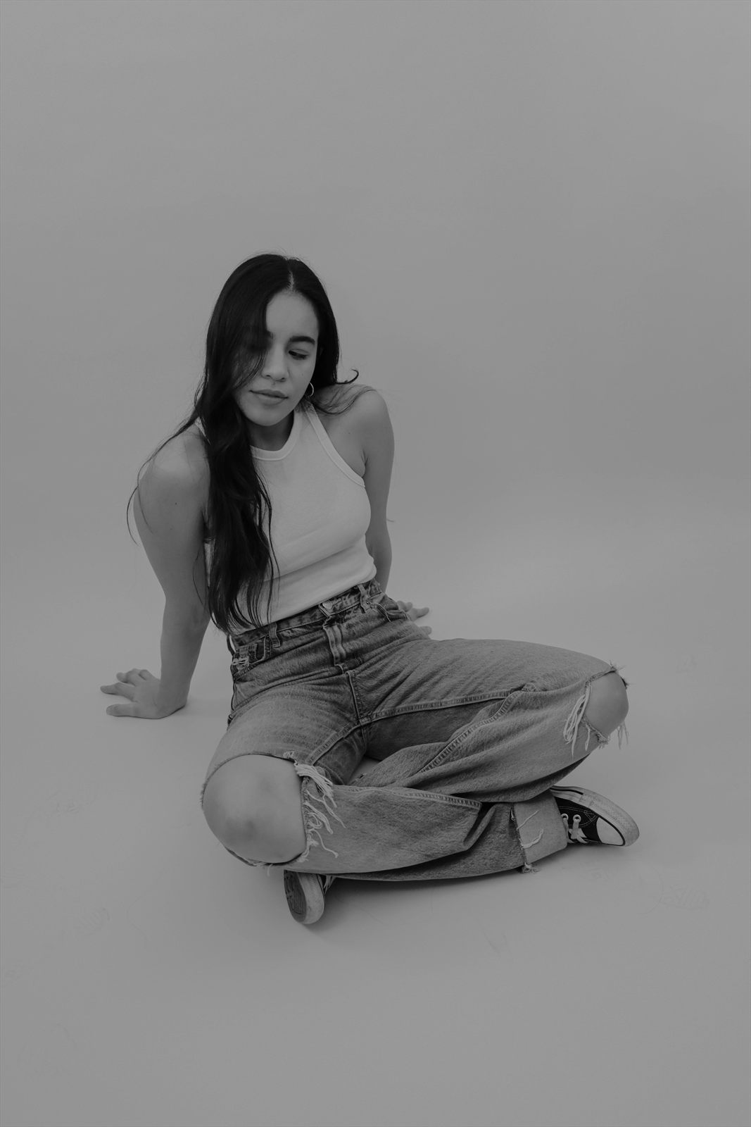 Retrato de estudio en blanco y negro, sentado en el piso sobre fondo liso